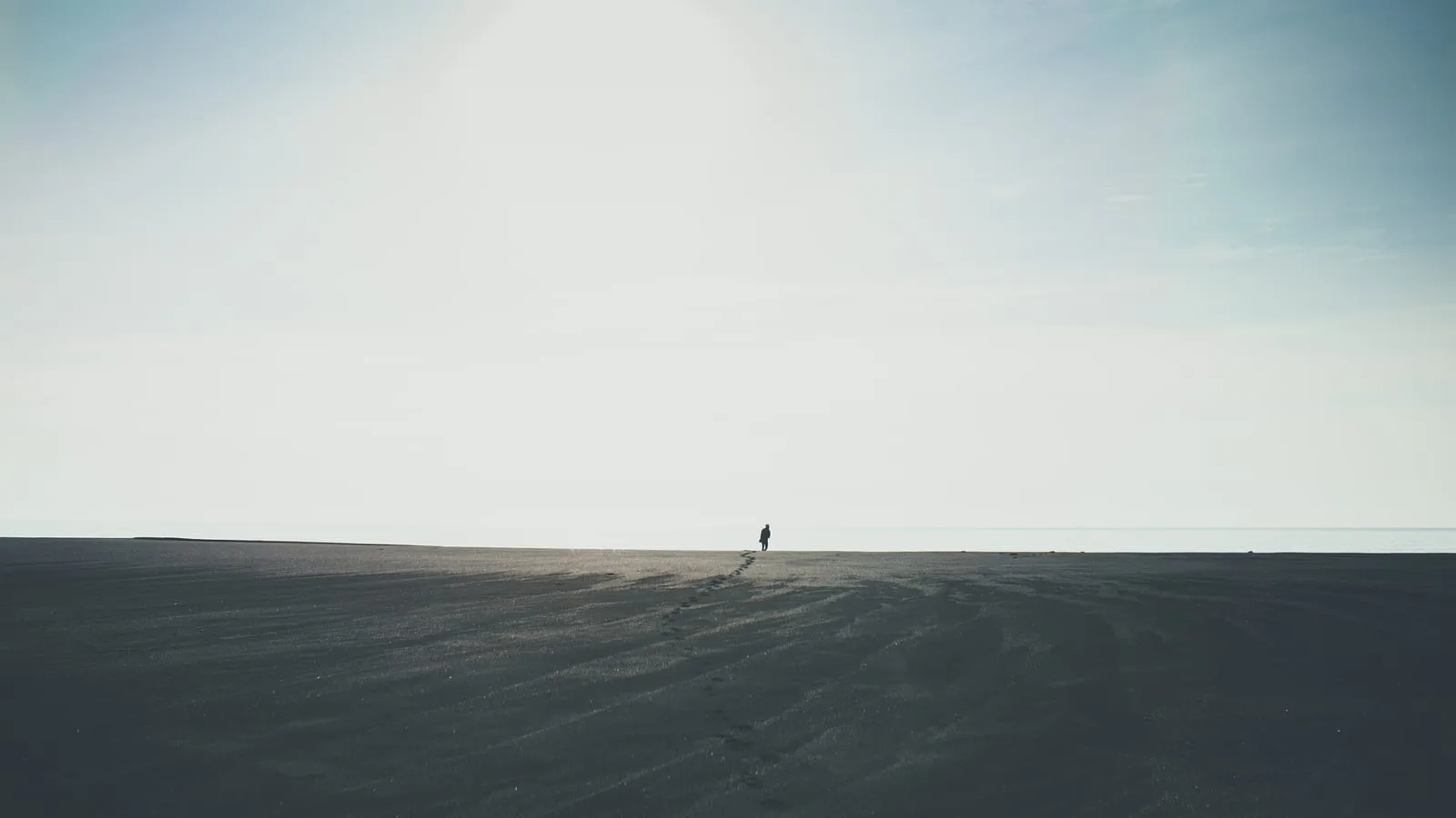 A lone figure walking toward the horizon across a vast, open landscape.